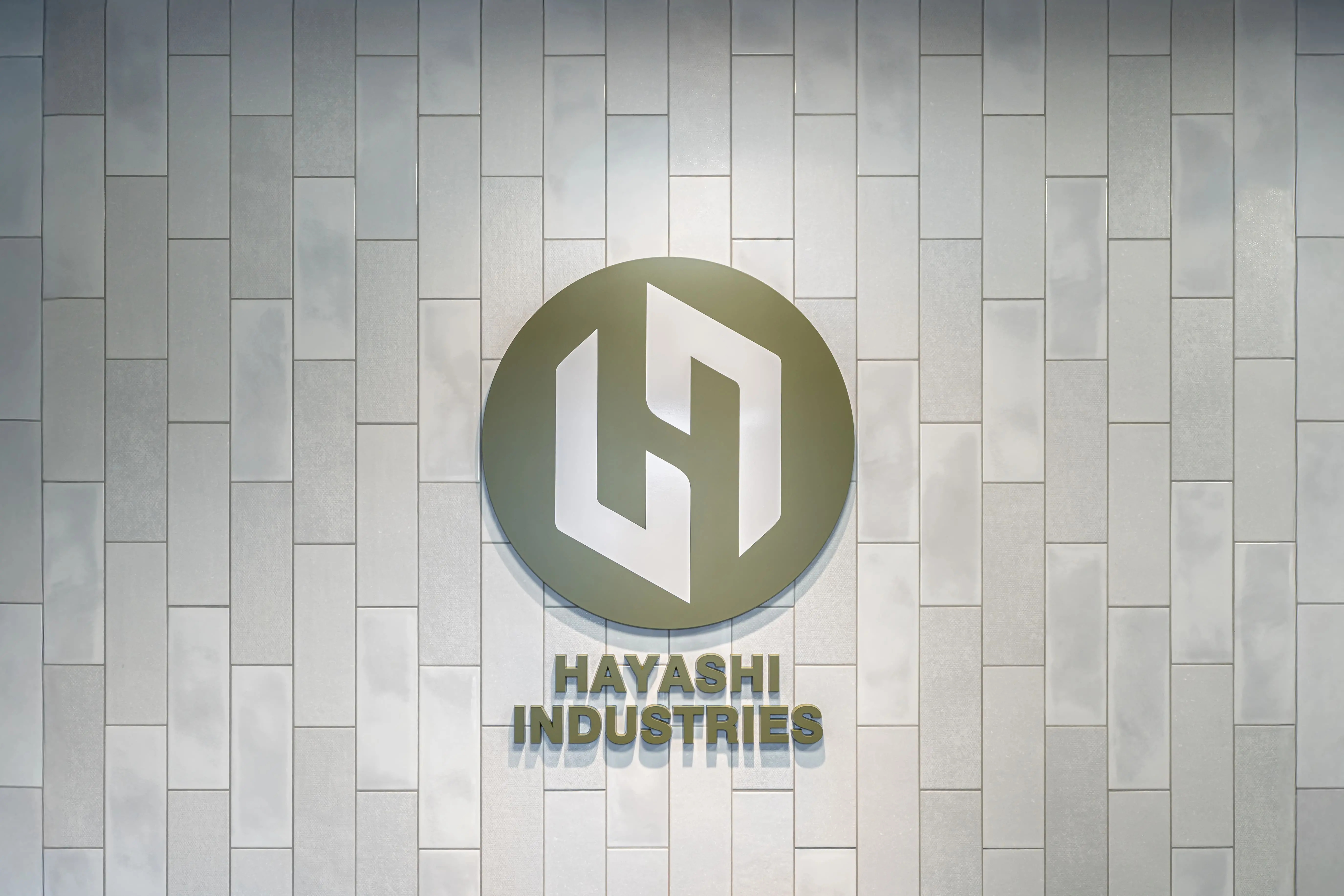 白いタイル壁に設置された緑色の円形ロゴと林工業株式会社の社名プレート