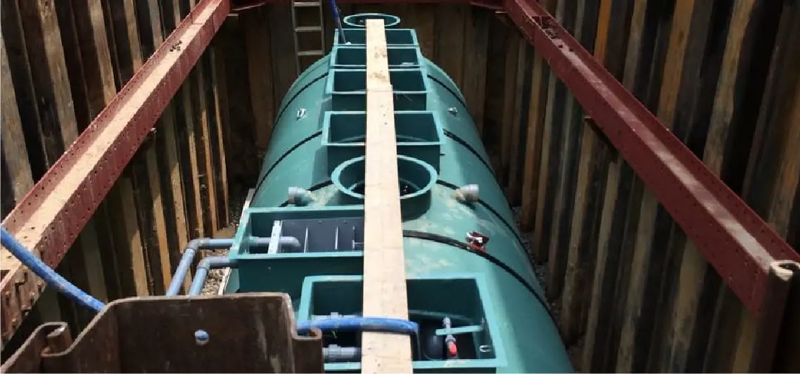 工事現場の深い溝に設置されている大型の青緑色の浄化槽と配管。浄化槽工事の様子