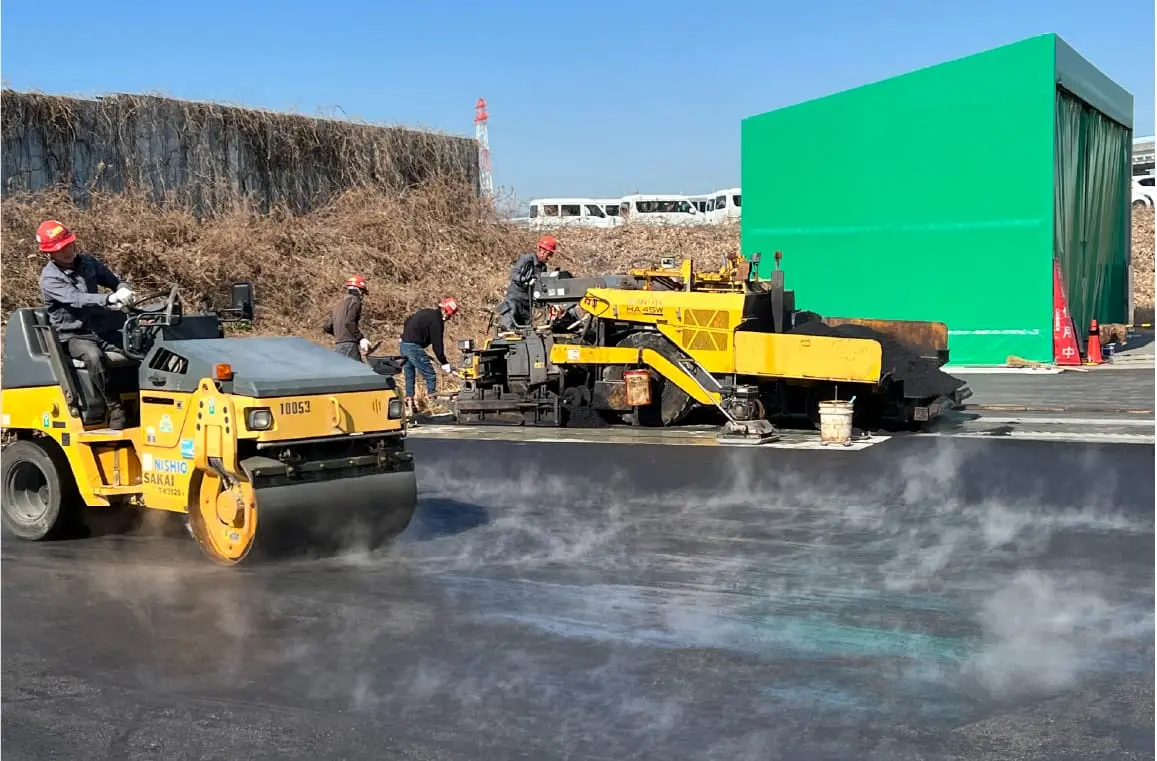 黄色いロードローラーとアスファルト舗装機械による道路舗装工事現場