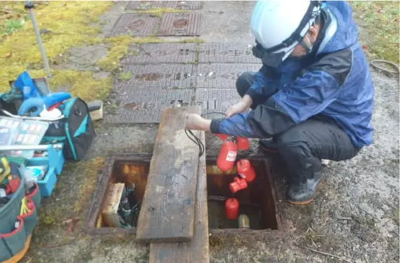 青い作業服を着た作業員が地面に設置された浄化槽の蓋を開けて点検作業を行っている様子