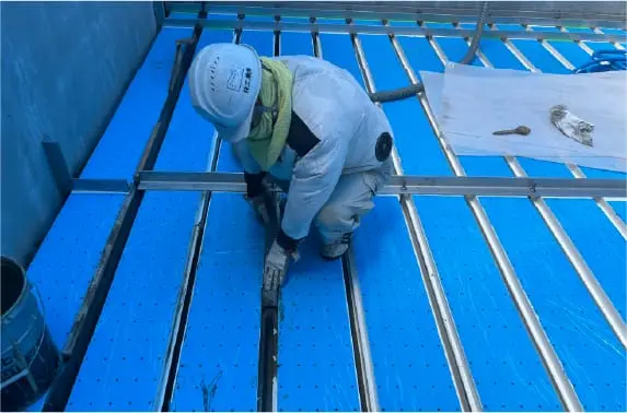 青色の防水塗装を施工中の作業員